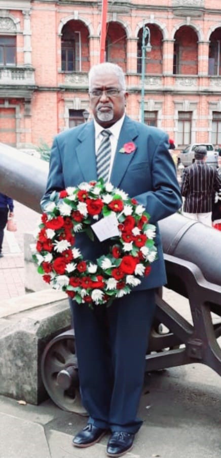 A person in a suit holding a wreath AI-generated content may be incorrect.